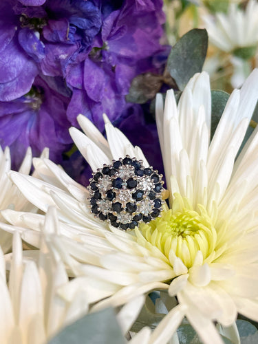 A diamond and sapphire flower cluster ring sitting on a white flower